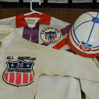 A hat with a sticker reading "26th Annual All-American Soap Box Derby", a sweater with a patch reading "All American 36 Soap Box Derby", and a shirt with a patch reading "Champion Soap Box Derby 1963"